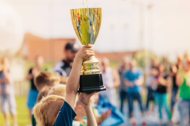 Okul takımındaki mutlu çocuklar altın kupayı yükseltiyorlar. Çocuklar spor şampiyonasını kazanıyor. Elinde büyük altın bir kupa tutan çocuk