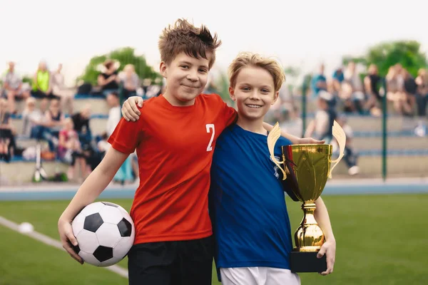 Счастливые два мальчика, как футболисты, зависающие на травяном поле. Дети с футбольным мячом и золотым кубком — стоковое фото