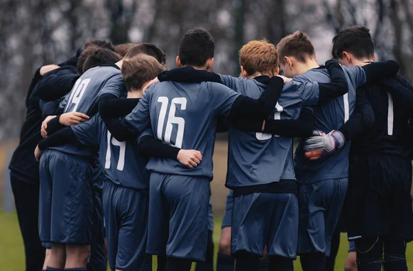 Soccer team with junior coach gathering together in a circle, to strategize and motivate. Football youth team standing together outdoor on grass pitch