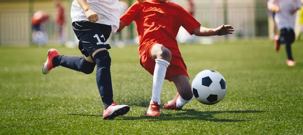 Sports players in football duel run. Footballers running fast and kicking soccer ball on grass stadium during school tournament match — Zdjęcie stockowe