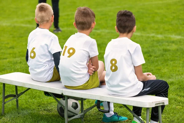 スポーツサッカーチームの少年たちがベンチに腰を下ろしている ジュニアレベルのスポーツ競技会トーナメントへの出場 サッカーベンチでのバックビュー — ストック写真