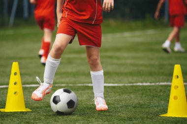 Futbol takımındaki çocuklar toplarla egzersiz yapıyor. Maçtan önce takım çalışması sırasında genç sporcular. Kırmızı spor giyimli genç oyuncular top ve sarı koni ile egzersiz yapıyorlar.