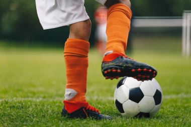 Futbol topu tekmesi. Kırmızı çoraplı ve kramponlu futbolcunun bacaklarına ve ayaklarına yakın dur ve topla koşup salya sür. Futbolcu topun peşinden koşuyor. Arka planda spor sahası ve futbol golü