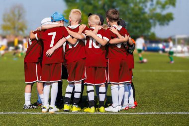 Spor takımındaki çocuklar okul futbol sahasında. Okul takımında spor yapan çocuklar. Çocuklar Turnuva Maçı 'ndan önce birbirlerine sokulup motive oluyorlar. Kırmızı Jersey formalı oyuncular