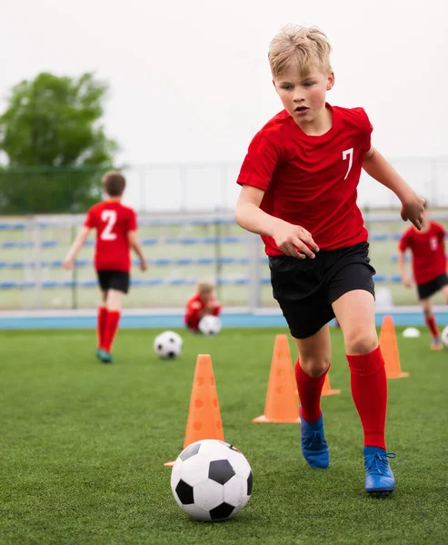Soccer Boy on Training with Ball and Soccer Cones. Dribbling Drill. Soccer Kids Dribble Training. Youth Soccer Club Practice Session. Boys in Sports Team in Red Soccer Uniforms