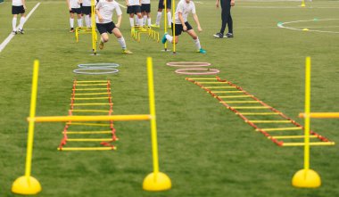 Antrenman ekipmanlı futbol sahası ve arka planda koçu olan oyuncular. Küçükler futbol takımı antrenmanı ve koç. Spor takımı antrenmanda. Futbol eğitim ekipmanları: merdiven, hula hoop, engel, koni