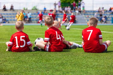 Genç Seviye Çocuklar Spor Takımı Çimen Sahasında Oturuyor. Futbol Futbolu Çocuk Oyuncuları Okul Futbol Yarışması sırasında Birlikte Ayakta Duruyorlar. Erkekler Red Soccer Jersey Spor Giyim ve Futbol Kramponlarında