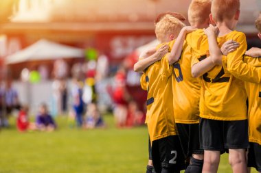 Sarı altın formalı çocuklar koçla moral konuşması yapıyor. Antrenör tarafından motive edilen çocuk futbol takımı. Futbol takımı koçluğu. Birlikte duran genç oğlanlar