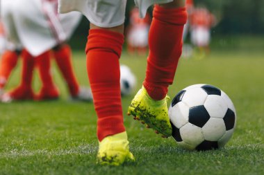 Futbolcular ayaklarınızı yakın tutun. Çimen tarlasında spor eğitimi. Spor giysili çocuklar. Kırmızı çorap ve krampon giyen oyuncular. Futbolun yatay arka planı. Futbol tekmesi.