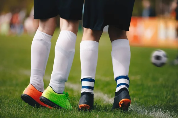 Soccer free kick wall - close up of players legs. Two young football players standing in wall during free kick. Kicked soccer ball in motion in the background. Players jumping up on grass field