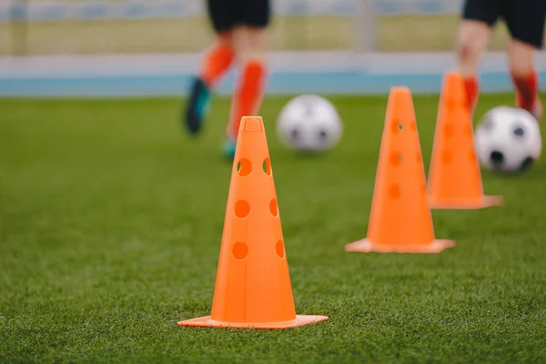 Sports training cones on soccer pitch. Players practice dribbling and passing skills on the grass field. Sports summer camp for young athletes