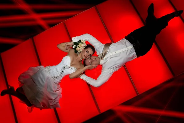 Bride and groom lying on red floor — Stock Photo, Image