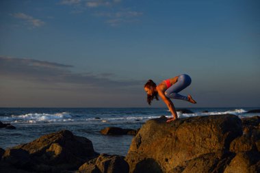 Uzun saçlı, yoga yapan genç bir kadın Mui Ne, Vietnam 'da kayalıklarda bakasana pozu veriyor..