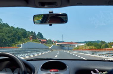 Asphalt otoyolu hareket halindeki bir araçtan görünen bir arazide.