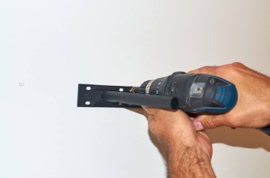 Adamın elleri duvara vida tabancasıyla raf tutacağıyla düzüşüyor. Yakın plan.