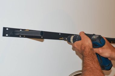 Adamın elleri duvarda bir raf tutacağıyla düzüşüyor. Yakın plan.