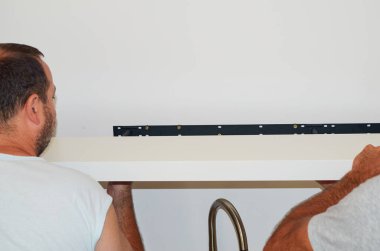 Erkekler bir rafa raf tutacağı yerleştiriyorlar. Duvara yakın plan.