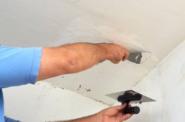 Man putting spackle on a ceiling during renovating works clipart