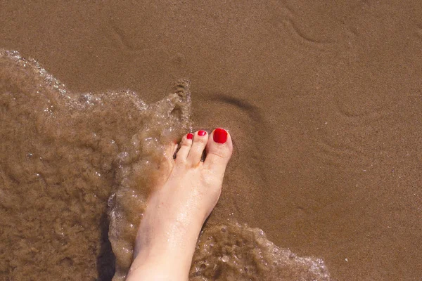 Pés de mulher com unhas pintadas de vermelho na areia do mar — Fotografia de Stock