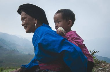 Guilin, Çin - 15 Haziran 2015: grand çocuklarını taşıyan bir büyük anne fotoğrafını bir sabah için onu geri yürümek paddy Teras Guilin Çin'de.