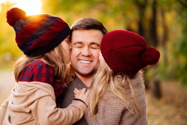 Bu sonbahar sokağında şapkalı iki kızı olan baba. Çocuklar babayı yanağından öpüyor..