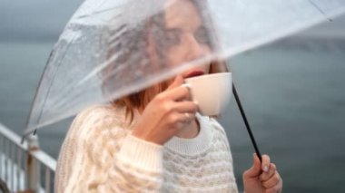 Kızıl saçlı kız şemsiyenin altında kahve içiyor.