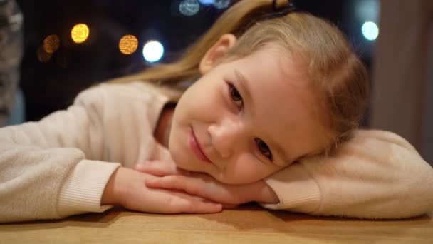 Petite fille couchée la tête sur la table et regardant la caméra . — Video