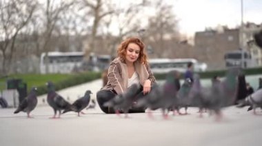 The girl sits in the square and feeding pigeons