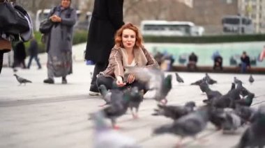 The girl sits in the square and feeding pigeons