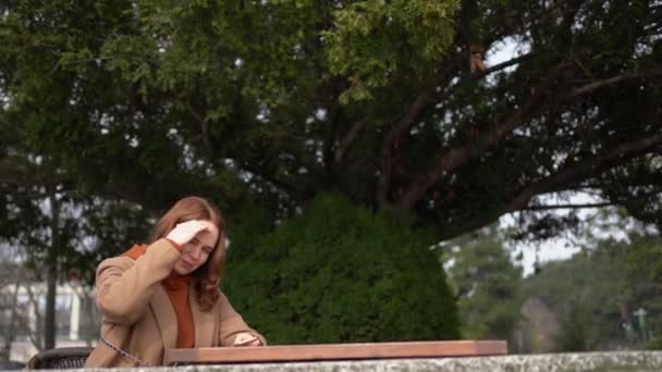 Девушка с каштановыми волосами сидит в кафе на улице — стоковое видео