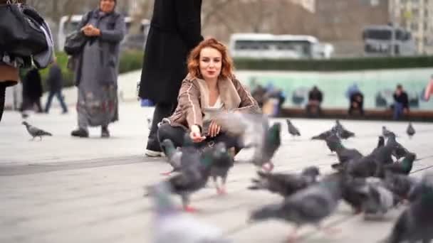 A menina senta-se na praça e alimentando pombos — Vídeo de Stock