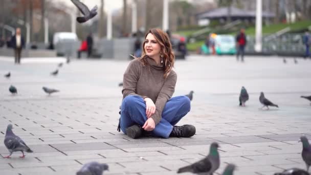 Девушка сидит на площади и вокруг голубей — стоковое видео