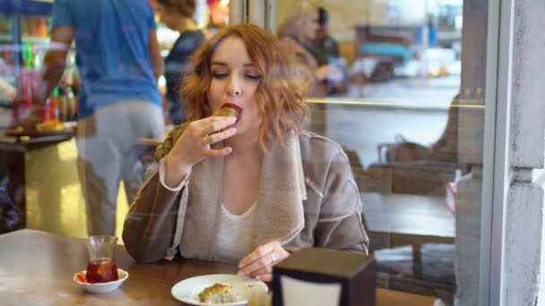 Rödhårig tjej på caféet äter sötsaker — Stockvideo