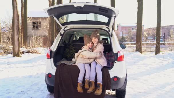 Two sisters sitting in the trunk of a car and hug — ストック動画