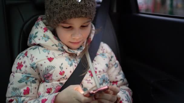 Klein meisje in de winter hoed en jas in de auto spelen telefoon. — Stockvideo