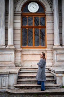 a girl stands on the steps of an old building in the rain
