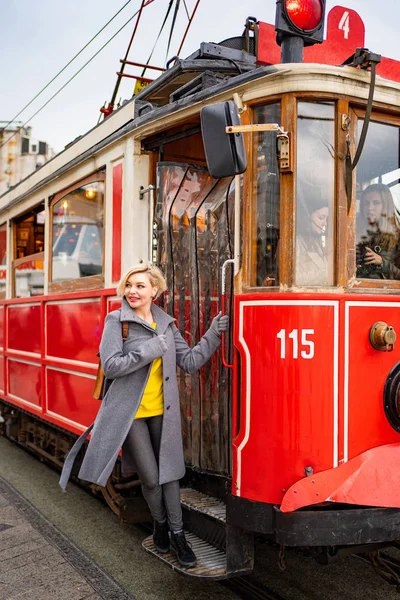 Blond girl in coat stand running Board red tram — Zdjęcie stockowe
