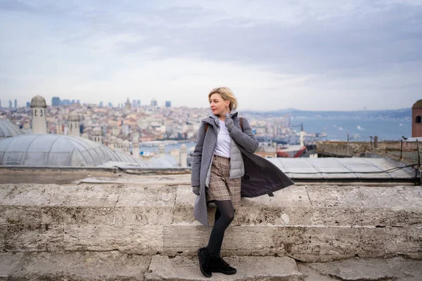 Ξανθιά με γκρι παλτό στέκεται ενάντια στις στέγες Κωνσταντινούπολη — Φωτογραφία Αρχείου