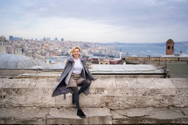 Blonde in grey coat sit against roofs  Istanbul — Φωτογραφία Αρχείου