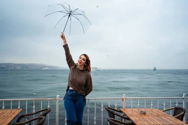 Κορίτσι γελάει στέκεται κάτω από μια ομπρέλα δίπλα στη θάλασσα — Φωτογραφία Αρχείου