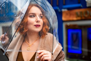 Şemsiyenin altında kızıl saçlı kahverengi elbiseli kız. 