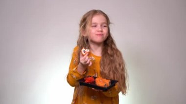 Little girl bites tasty rolls and holds in hands.