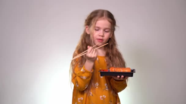 La bambina lecca i bastoncini di sushi e tiene i rotoli di scatola — Video Stock