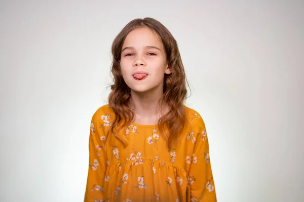 A teenage girl shows her tongue in an orange dress — 스톡 사진