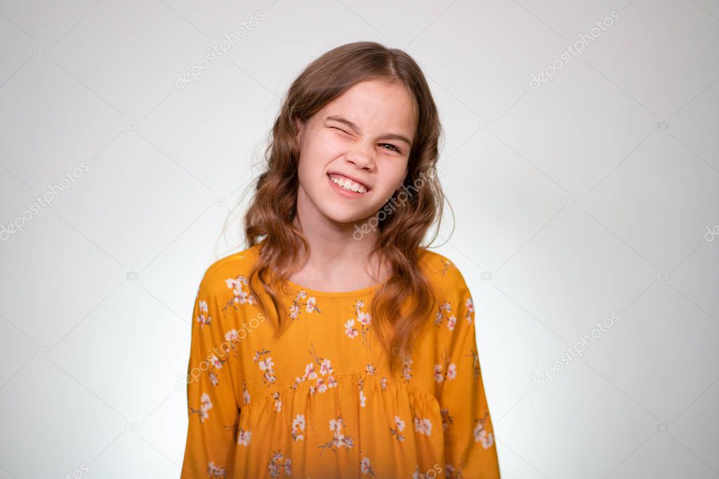A teenage girl winks one eye in an orange dress.