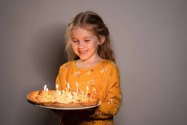 Klein meisje holding pizza met kaarsen kijkt vuur — Stockfoto