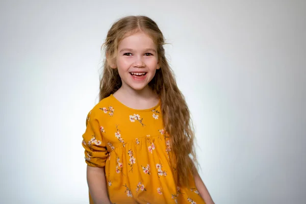 Kleines Mädchen in gelbem Kleid lacht auf weißem Rücken — Stockfoto