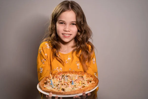 Ein Teenie-Mädchen hält eine Pizza mit brennenden Kerzen — Stockfoto