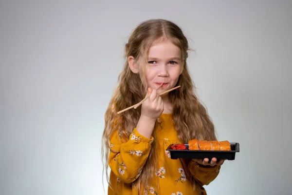 Little girl licks sushi sticks and keeps box rolls — Stockfoto