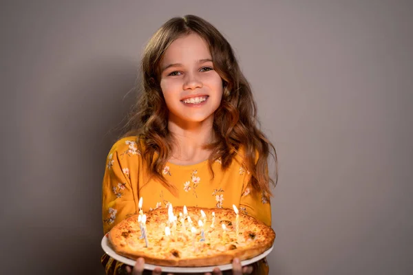 A teen girl holding pizza with candles is smiling — Stockfoto
